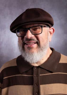 A man with glasses, a gray beard and wearing a hat.
